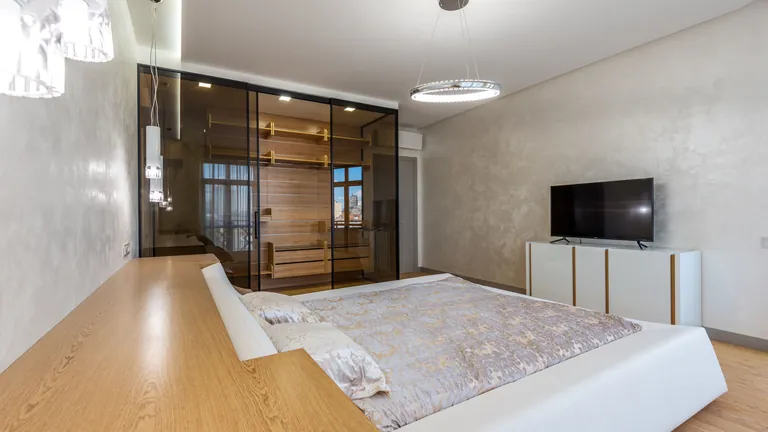 Smoked-glass partition doors beside warm timber joinery in a bedroom