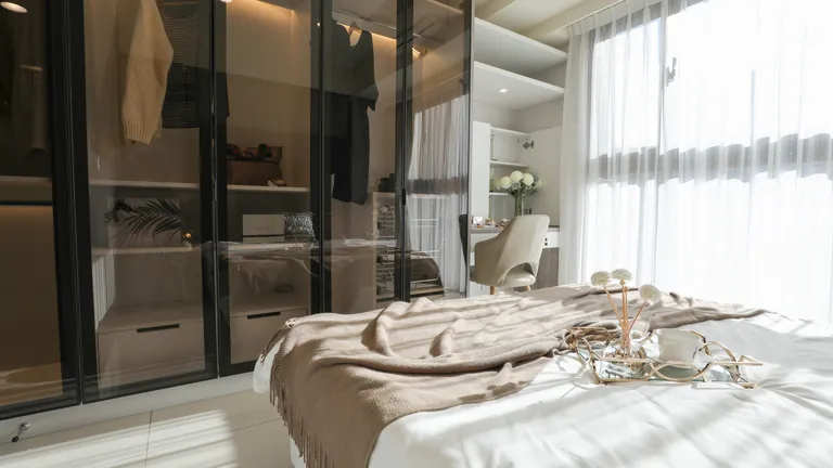 Glass-front wardrobe with slim aluminium frames in a beige bedroom